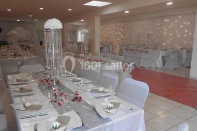 Salle de réception décorée avec des tables dressées, nappes blanches, chaises ornées de nœuds violets et centres de table…
