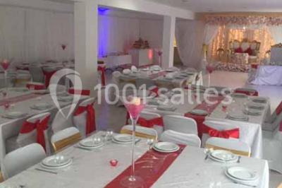 Salle de réception décorée avec des tables dressées, nappes blanches, chaises ornées de nœuds violets et centres de table…