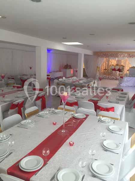 Salle de réception décorée avec des nappes blanches et rouges, tables dressées avec vaisselle et chaises ornées de rubans…