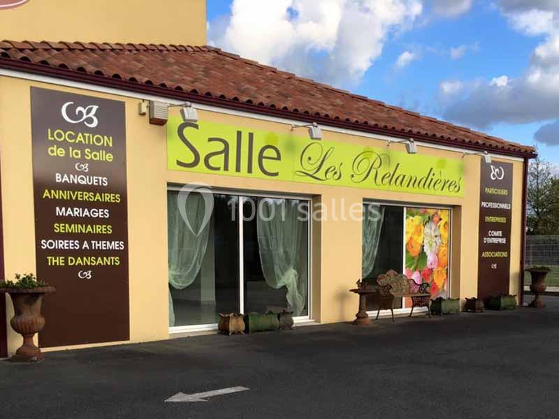 Façade d'une salle de réception avec enseigne ’Salle Les Relandières’ et panneaux indiquant les services proposés.