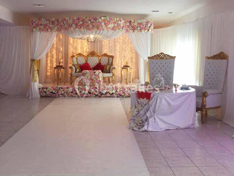 Décoration de salle de mariage avec arche fleurie, fauteuils dorés, table ornée et éclairage chaleureux.