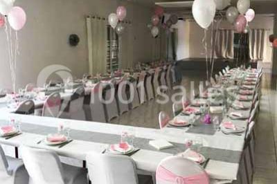 Salle de réception décorée avec des tables dressées, nappes blanches, chaises ornées de nœuds violets et centres de table…