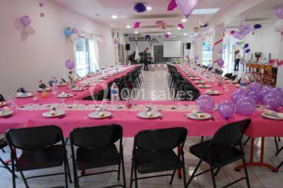 Salle de réception décorée avec des tables dressées, nappes blanches, chaises ornées de nœuds violets et centres de table…