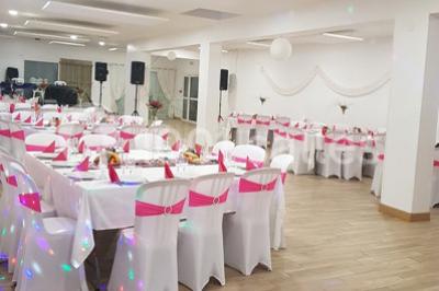 Salle de réception décorée avec des tables dressées, nappes blanches, chaises ornées de nœuds violets et centres de table…