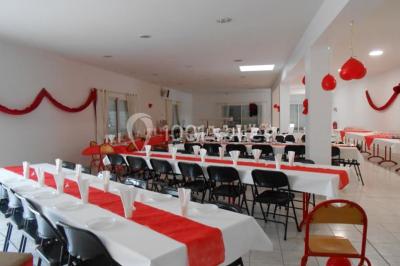 Salle de réception décorée avec des tables dressées, nappes blanches, chaises ornées de nœuds violets et centres de table…