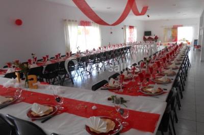 Salle de réception décorée avec des tables dressées, nappes blanches, chaises ornées de nœuds violets et centres de table…