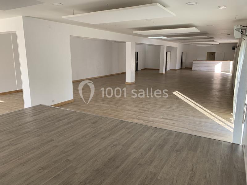Salle vide avec un sol en parquet, murs blancs, plafond avec panneaux acoustiques et un comptoir en arrière-plan.