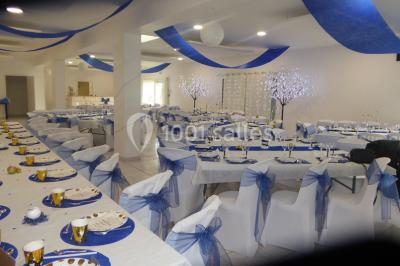 Salle de réception décorée avec des tables dressées, nappes blanches, chaises ornées de nœuds violets et centres de table…