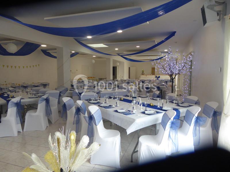 Salle de réception décorée avec des nappes blanches, des rubans bleus et des lumières d'ambiance.