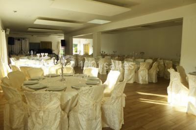 Salle de réception décorée avec des tables dressées, nappes blanches, chaises ornées de nœuds violets et centres de table…