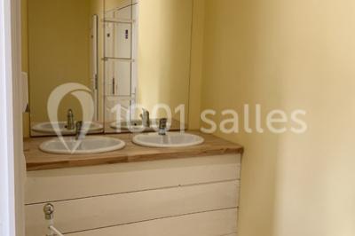 Salle de réception décorée avec des tables dressées, nappes blanches, chaises ornées de nœuds violets et centres de table…