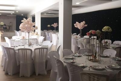 Salle de réception décorée avec des tables dressées, nappes blanches, chaises ornées de nœuds violets et centres de table…