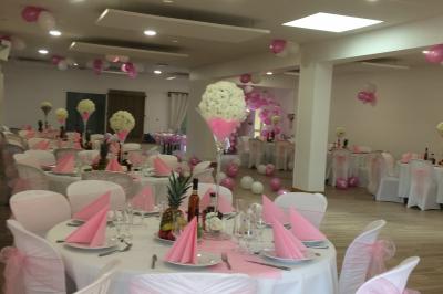 Salle de réception décorée avec des tables dressées, nappes blanches, chaises ornées de nœuds violets et centres de table…