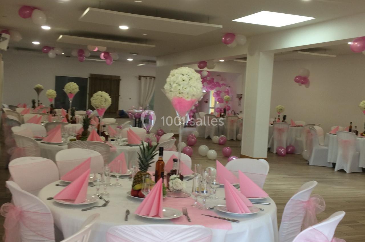 Salle de réception décorée avec des nappes blanches, des serviettes roses et des ballons assortis pour un événement festif.