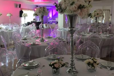 Salle de réception décorée avec des tables dressées, nappes blanches, chaises ornées de nœuds violets et centres de table…