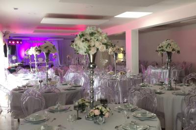Salle de réception décorée avec des tables dressées, nappes blanches, chaises ornées de nœuds violets et centres de table…