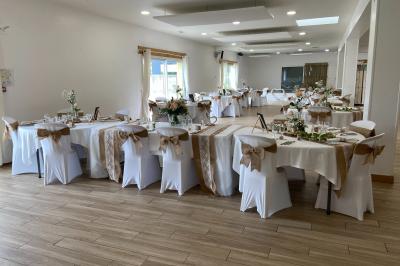 Salle de réception décorée avec des tables dressées, nappes blanches, chaises ornées de nœuds violets et centres de table…