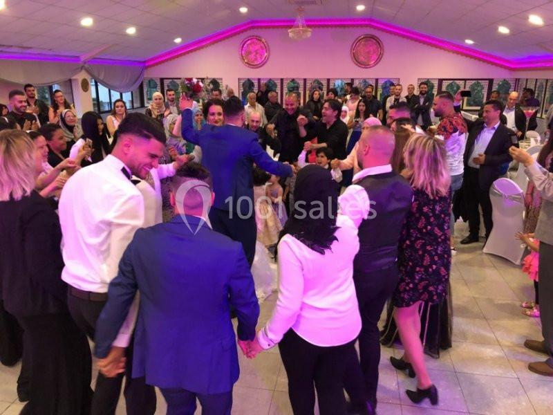 Des personnes dansent en cercle lors d'une fête dans une salle décorée avec des lumières colorées.