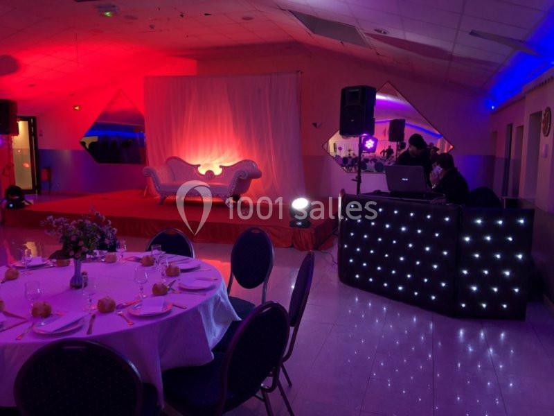 Salle de réception décorée avec une scène éclairée en rouge, une table dressée et une console de DJ illuminée.