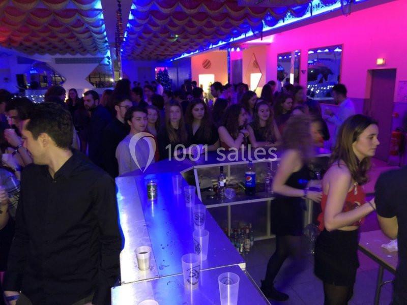 Des personnes rassemblées dans un bar animé, éclairé par des lumières colorées, avec des verres sur le comptoir.