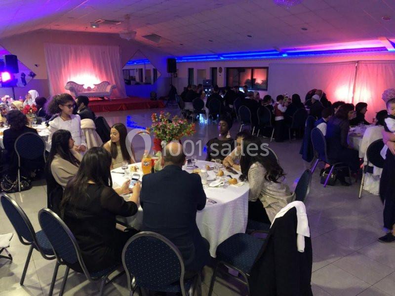 Des personnes assises autour de tables rondes dans une salle éclairée, décorée pour un événement festif.