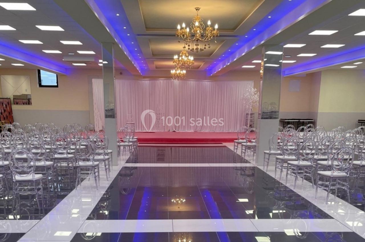 Salle de réception avec chaises transparentes alignées, lustres suspendus et éclairage coloré au plafond.