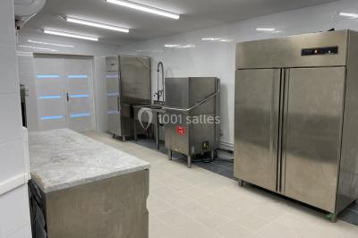 Cuisine professionnelle équipée avec lave-vaisselle industriel, réfrigérateur, plan de travail et cuisinière en inox.