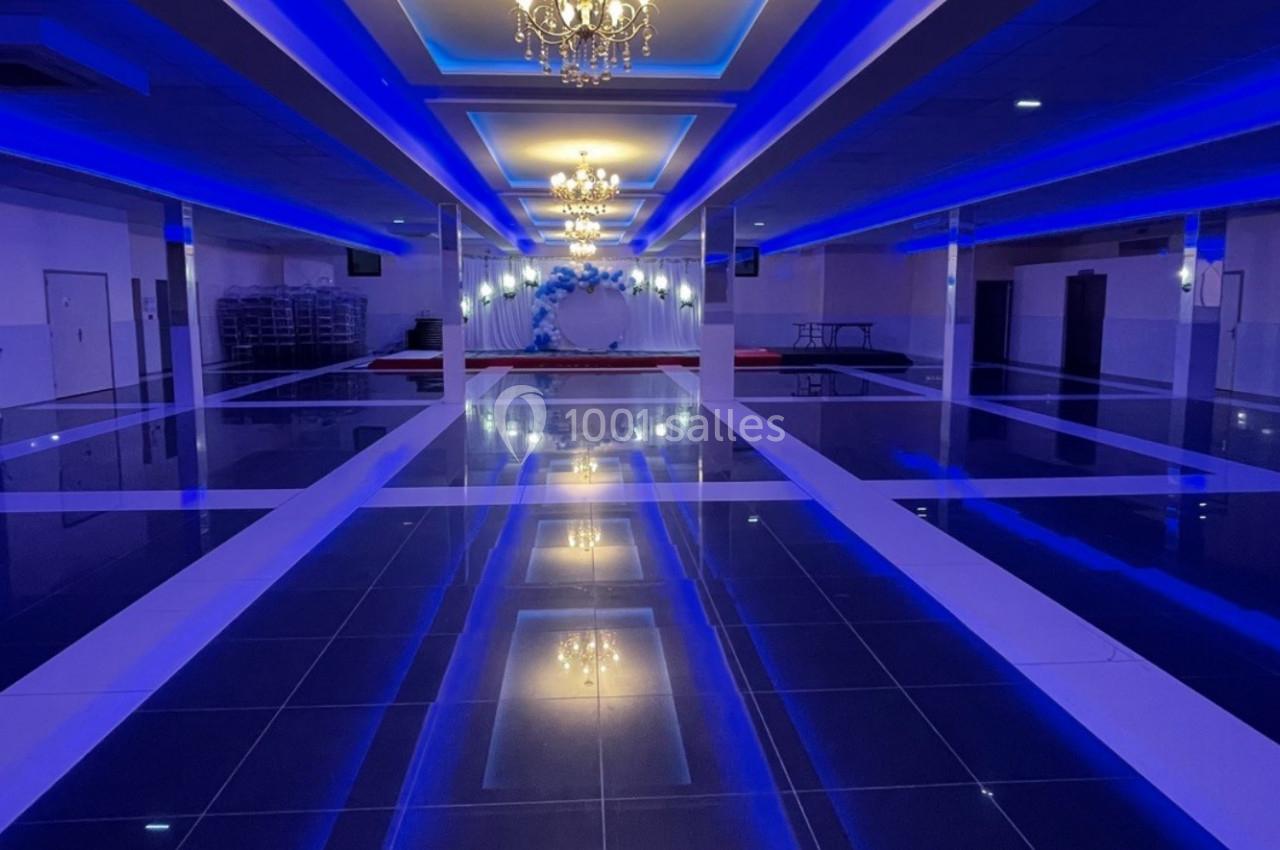 Salle de réception spacieuse avec éclairage bleu, lustres suspendus et sol brillant en carrelage noir.