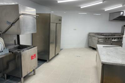 Cuisine professionnelle équipée avec lave-vaisselle industriel, réfrigérateur, plan de travail et cuisinière en inox.