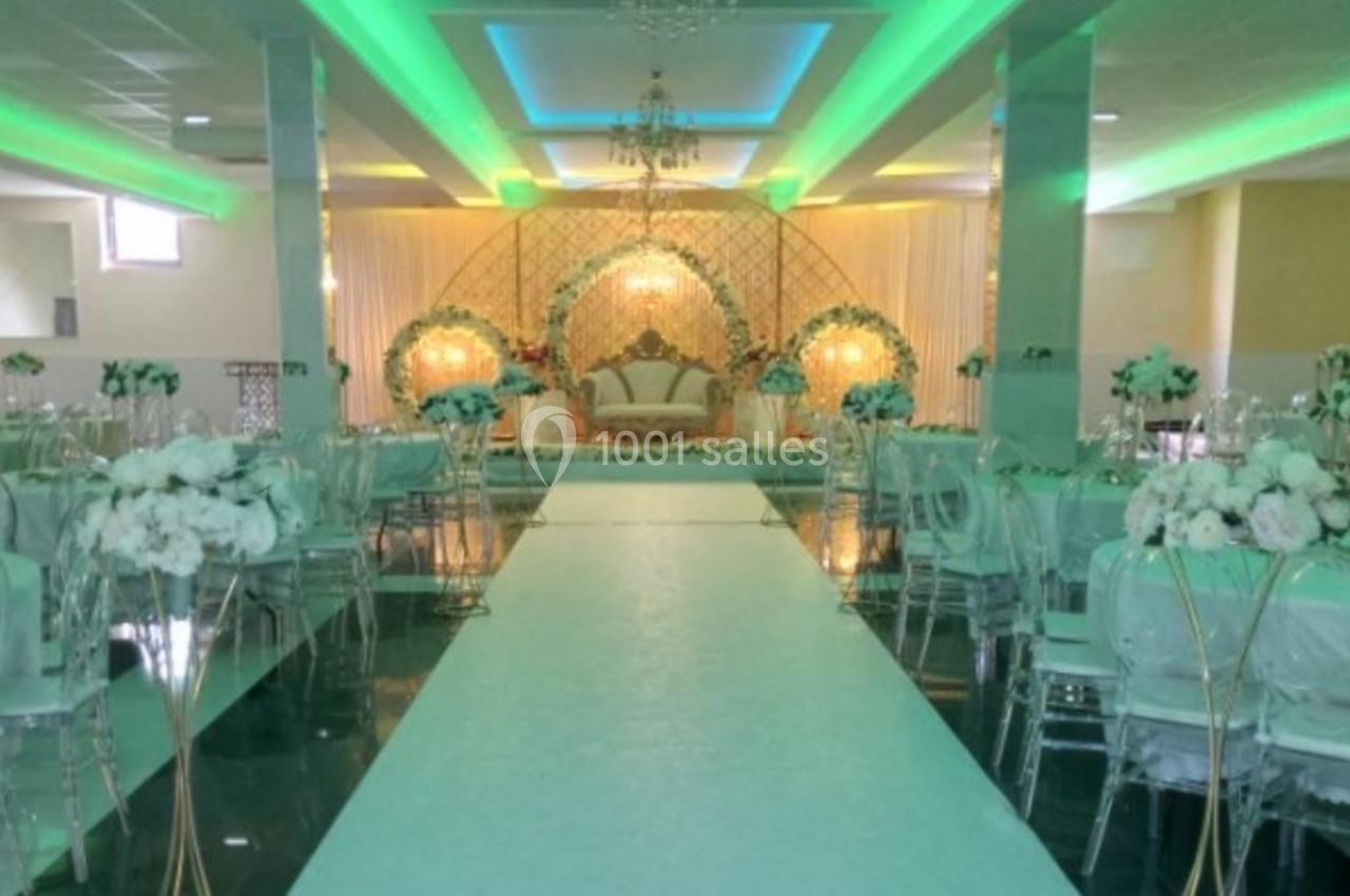 Salle de réception décorée avec des tons verts et blancs, comprenant des tables dressées et une scène ornée au fond.