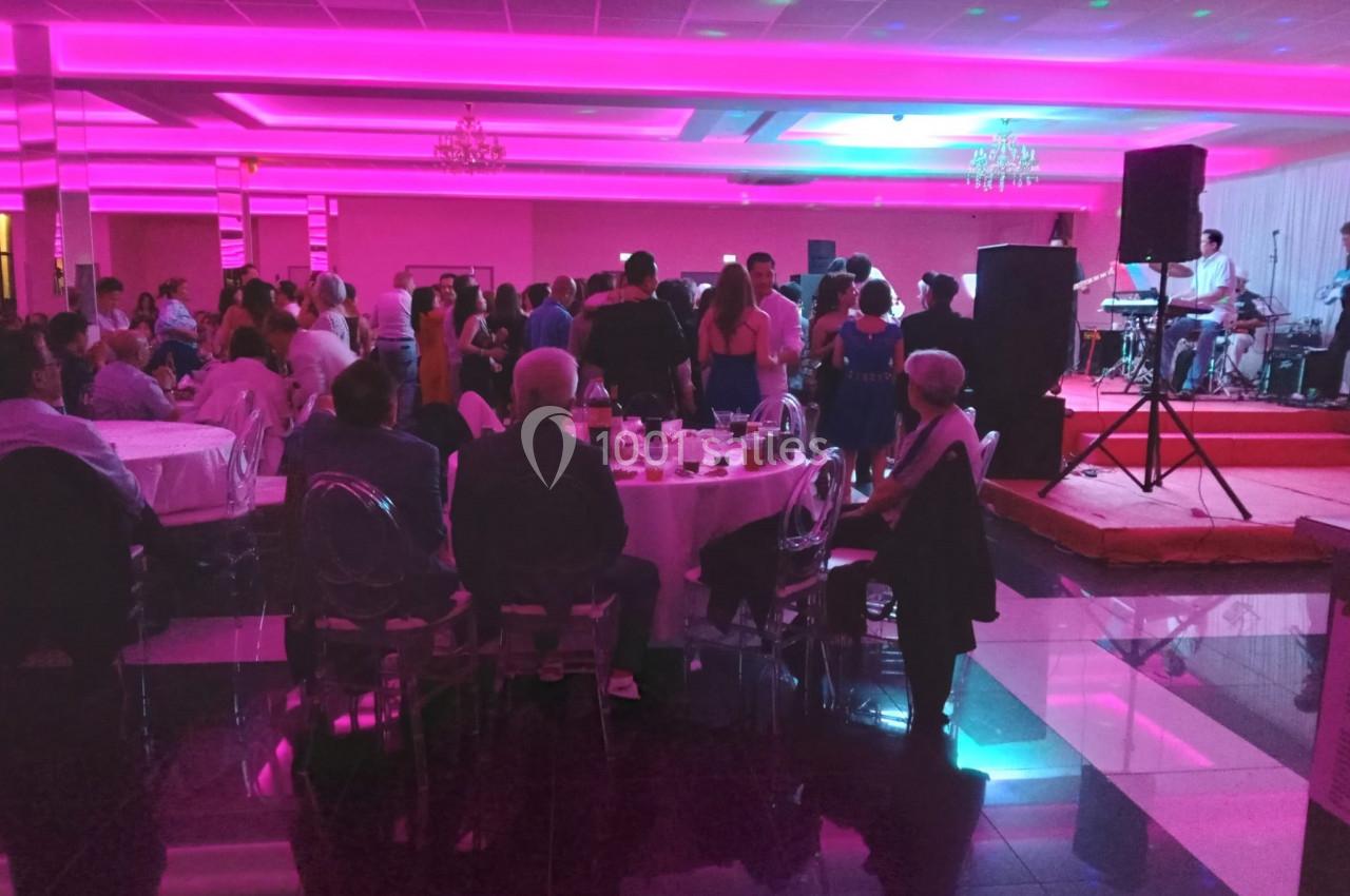 Salle de réception avec invités assis et debout, éclairée par des lumières roses, et un groupe jouant sur scène.