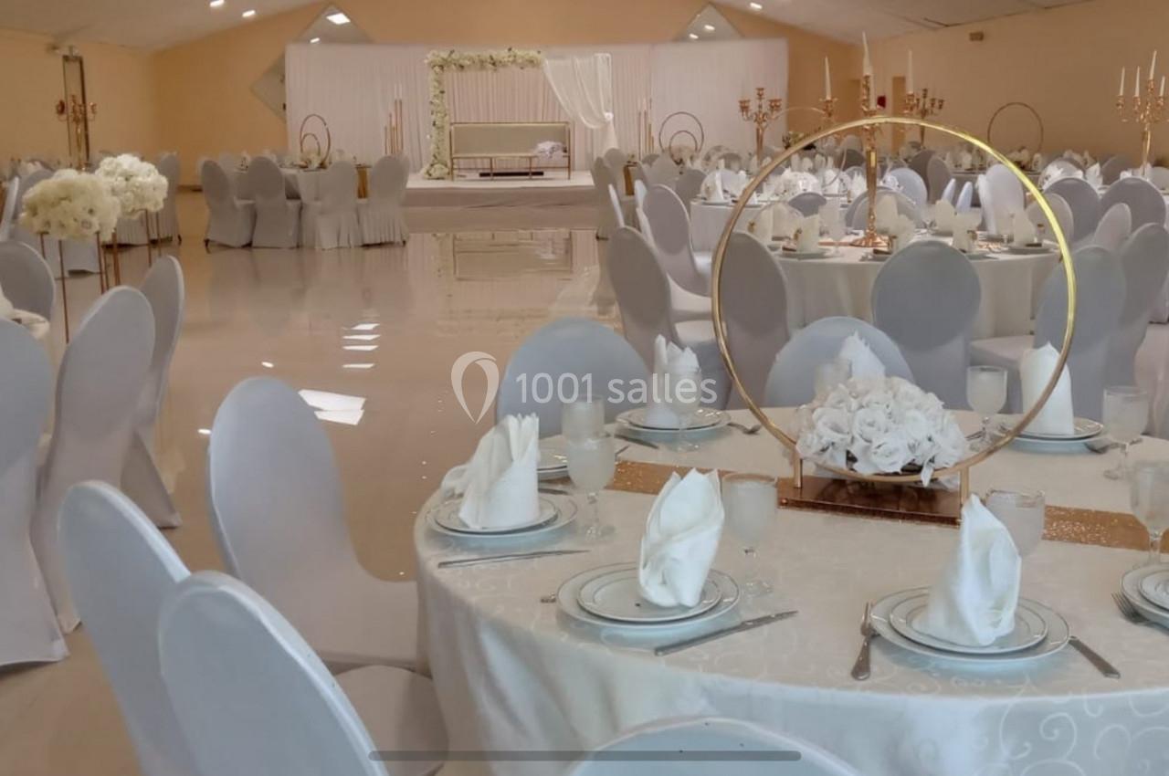 Salle de réception décorée avec des tables rondes, nappes blanches, serviettes pliées et centre de table floral.