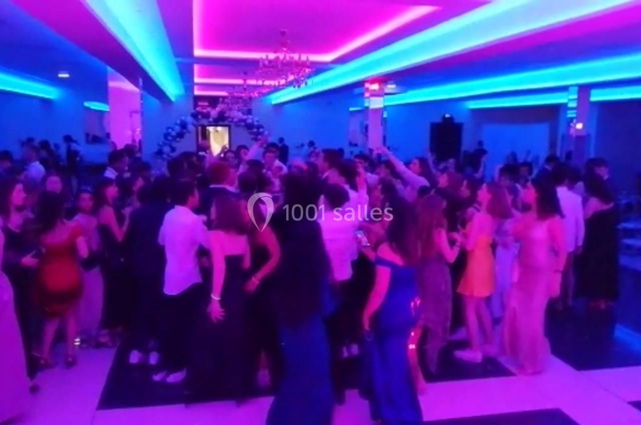 Groupe de personnes dansant dans une salle éclairée par des lumières colorées roses et bleues.