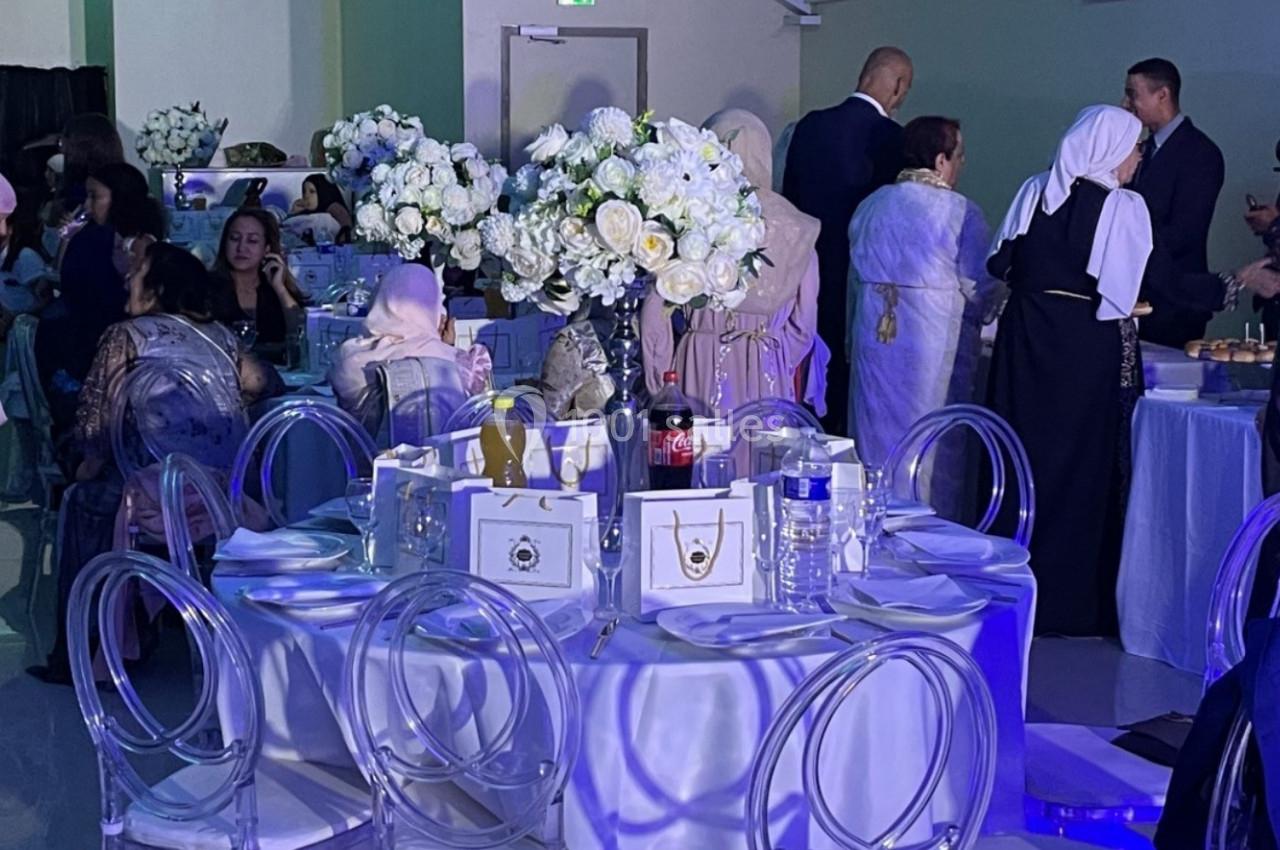 Des convives en tenue élégante participent à un événement dans une salle décorée avec des tables fleuries et éclairage…