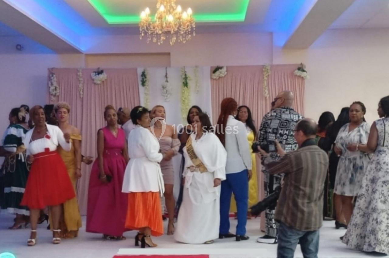 Groupe de personnes en tenue élégante rassemblées dans une salle décorée avec des rideaux roses et un lustre.