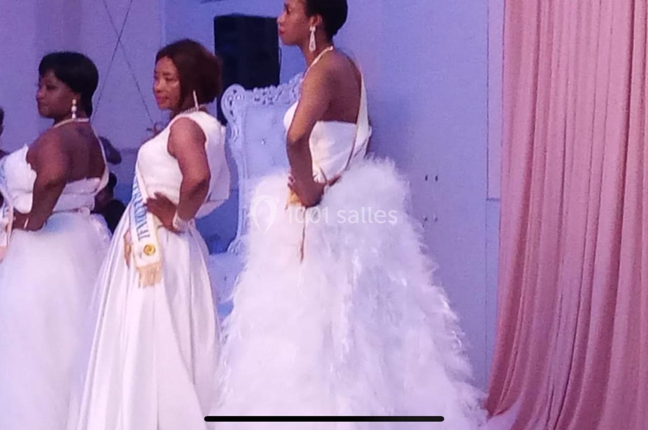 Trois femmes en robes de mariée posent sur une scène, avec un rideau rose en arrière-plan.