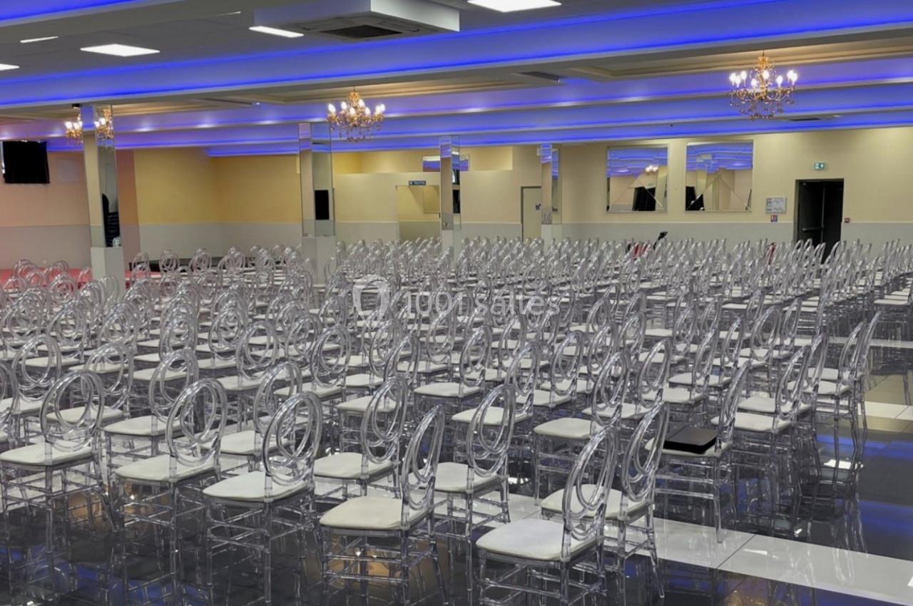 Salle de réception spacieuse avec des rangées de chaises transparentes et un éclairage bleu au plafond.