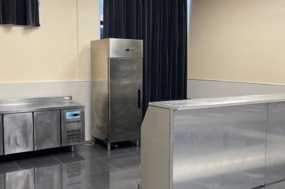 Cuisine professionnelle équipée avec lave-vaisselle industriel, réfrigérateur, plan de travail et cuisinière en inox.