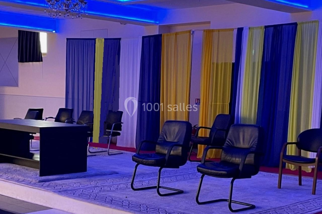 Salle de conférence avec des chaises noires disposées autour d'une table sur un tapis, éclairage bleu et rideaux colorés en…