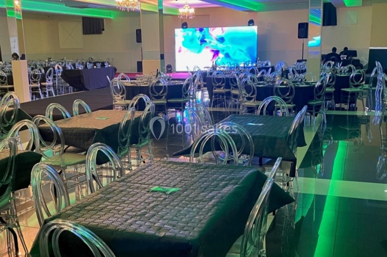 Salle de réception avec des tables couvertes de nappes sombres, des chaises transparentes et un écran lumineux en arrière…