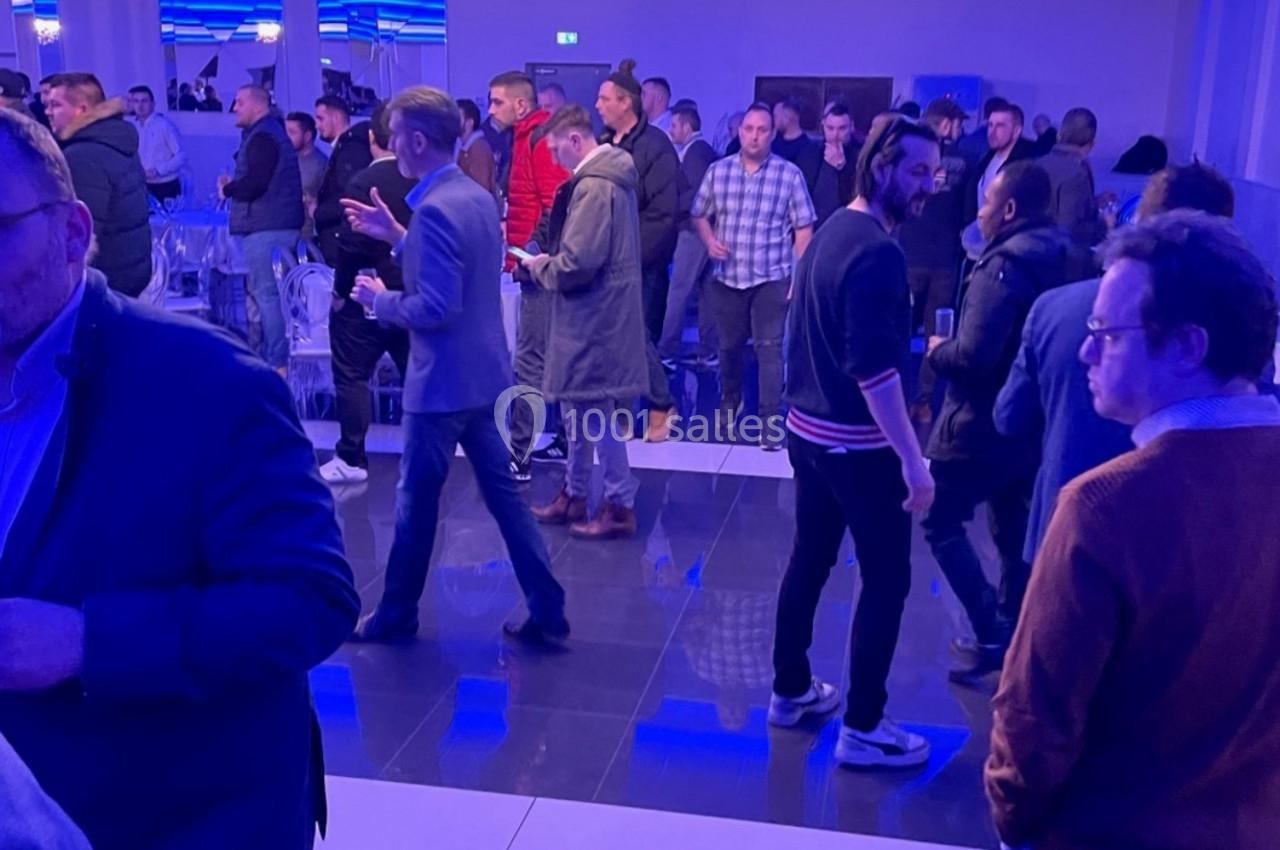 Groupe de personnes debout dans une salle éclairée en bleu, discutant près d'un buffet.