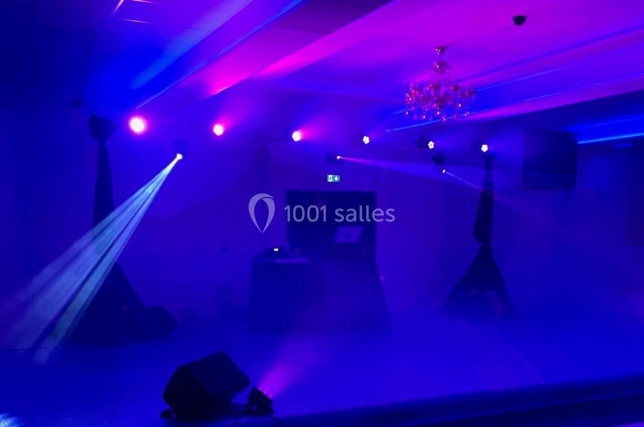 Salle de réception illuminée par des projecteurs colorés violets et bleus, avec une scène et un éclairage tamisé.