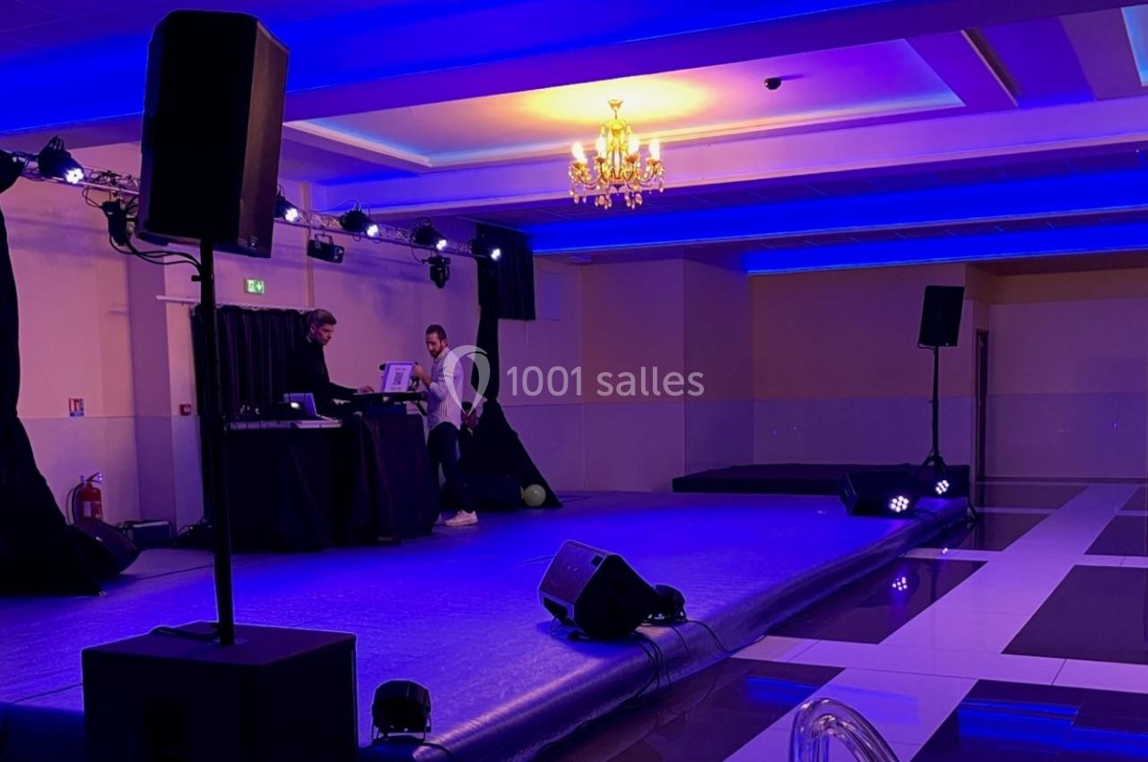 Salle de réception avec scène éclairée en bleu, équipement audio et deux personnes près d'une table de mixage.