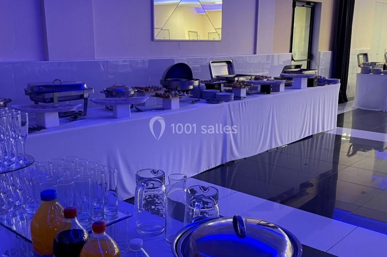 Buffet de réception avec plats chauds, verrerie, carafes et boissons disposés sur des tables drapées de blanc.