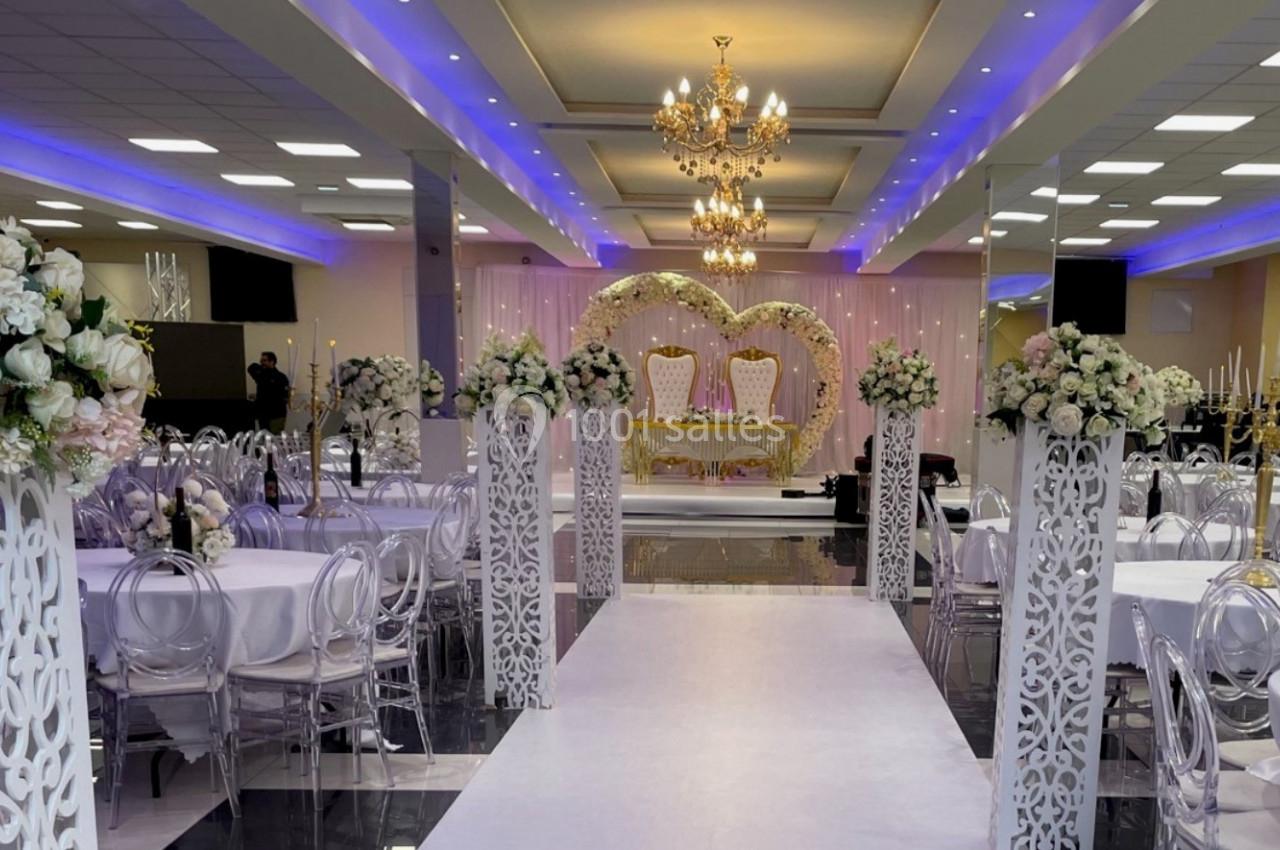 Salle de réception décorée avec des fleurs blanches, des chandeliers et une arche en forme de cœur au fond.