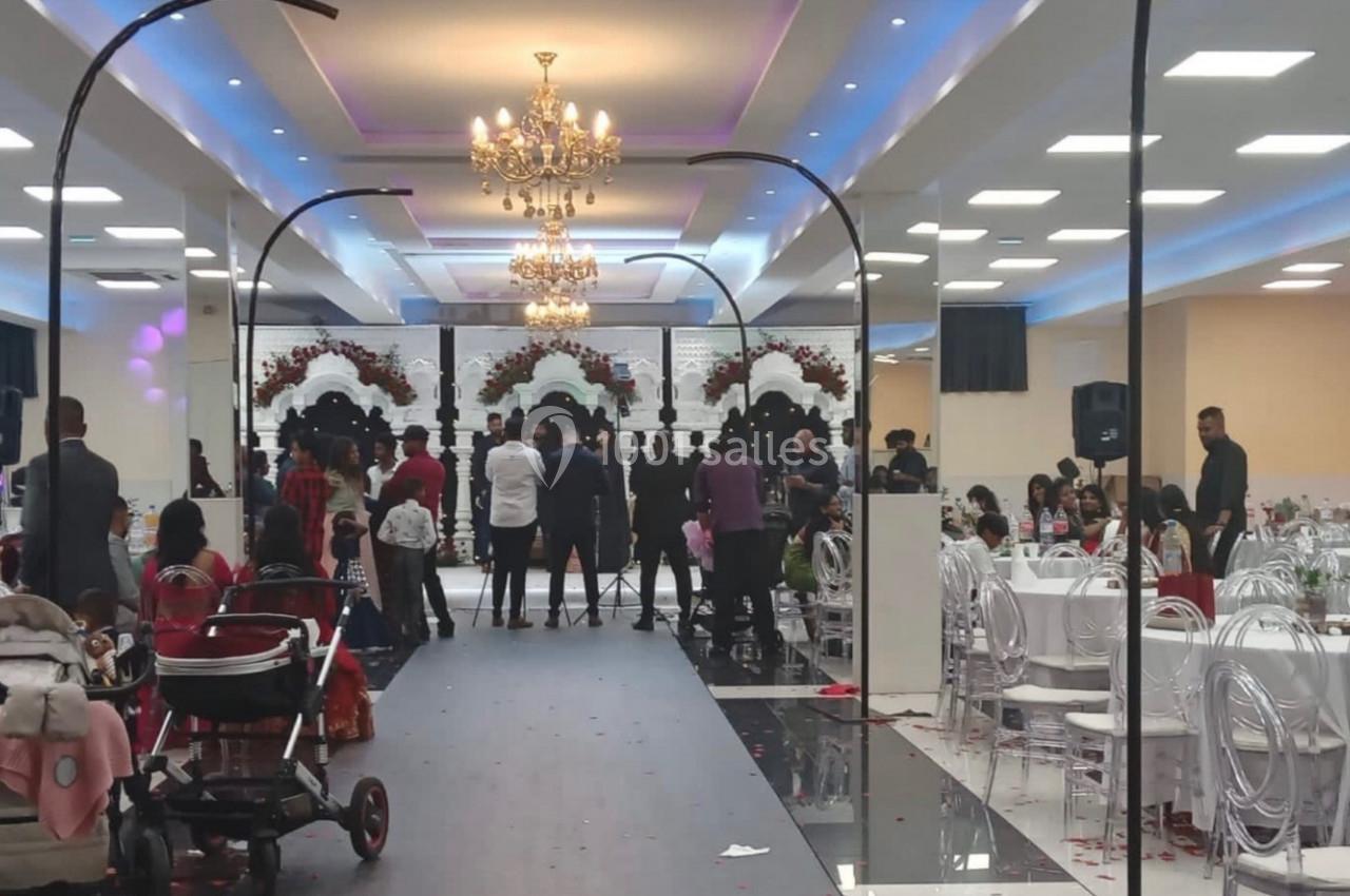 Salle de réception décorée avec des lustres, des tables dressées et des invités rassemblés près d'une scène.