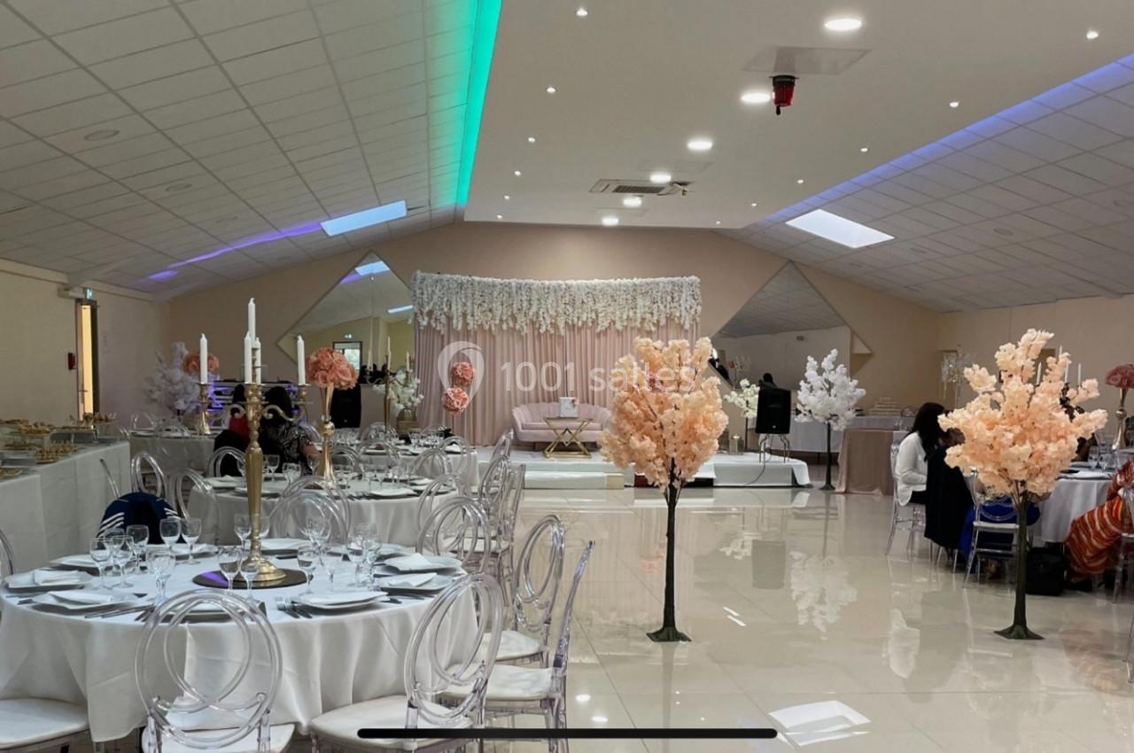 Salle de réception décorée avec des tables rondes, chaises transparentes et arrangements floraux roses.
