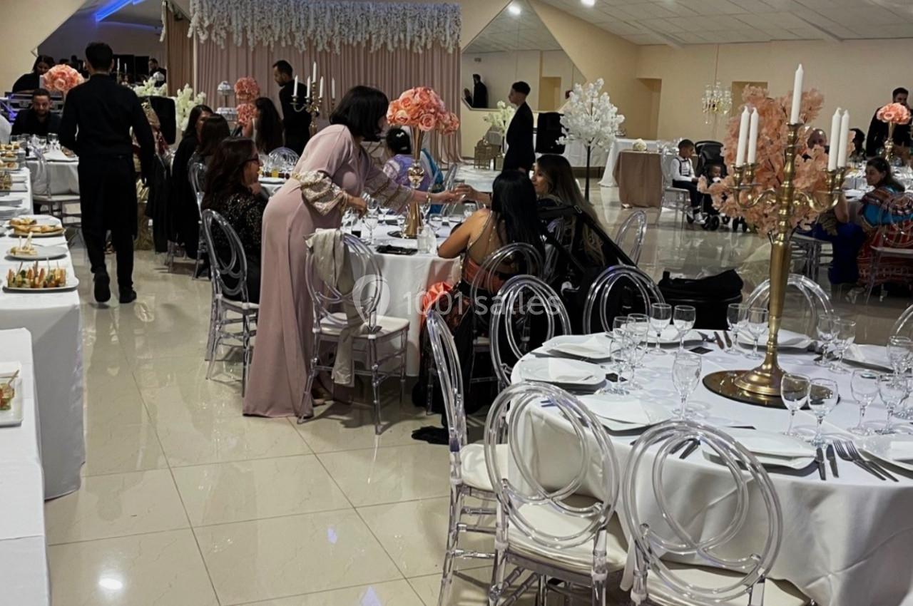 Salle de réception décorée avec des tables rondes, des chaises transparentes et des arrangements floraux, des invités assis…