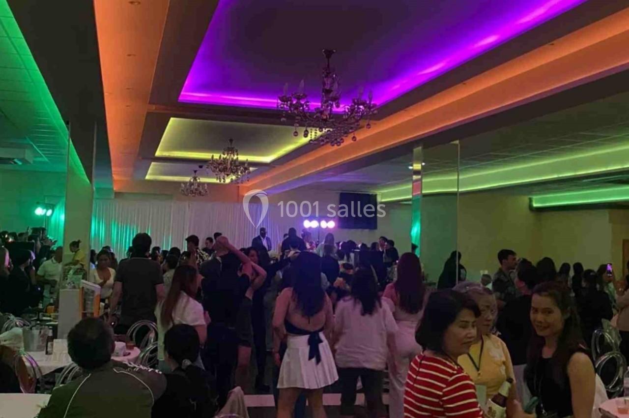 Salle de réception animée avec des invités dansant et discutant sous des éclairages colorés au plafond.