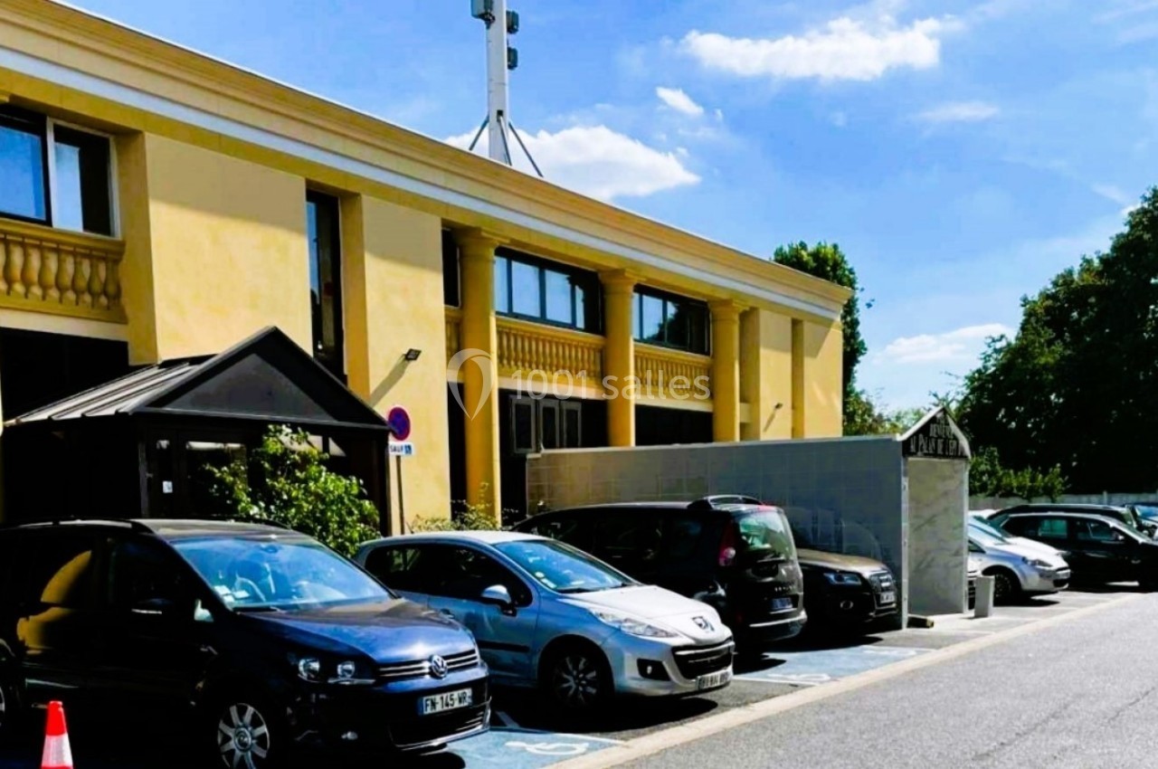 Stationnement avec plusieurs voitures garées devant un bâtiment jaune à colonnes, sous un ciel dégagé.